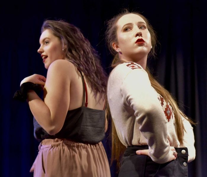 Two women back to back in the middle of a performance on stage