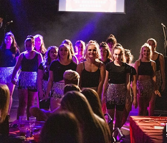 A large group of performing arts students looking directly to the camera in the middle of a production
