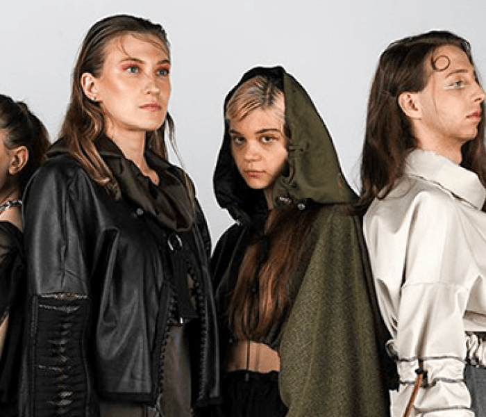 Four Fashion Design students stood posing back to back for a photoshoot against a grey wall