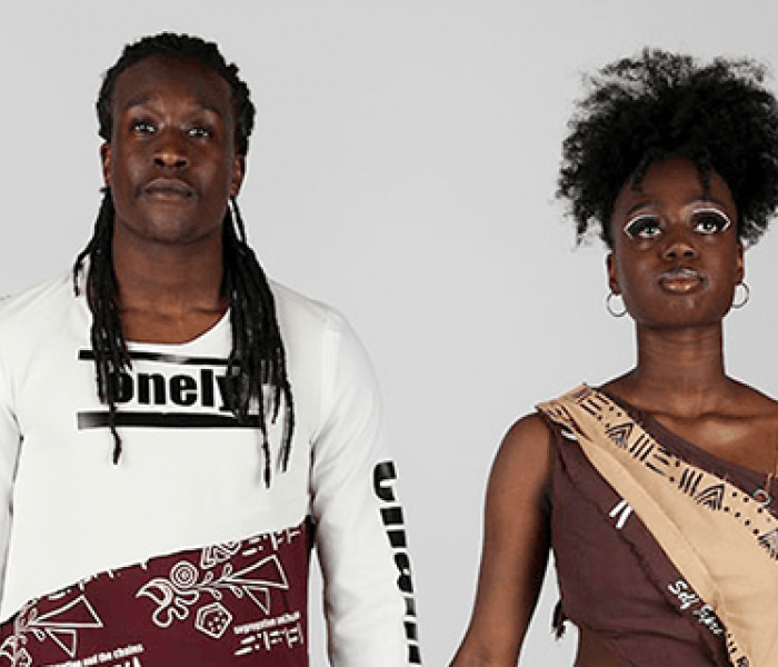 Two Fashion Design students stood side by side holding hands modelling their clothes