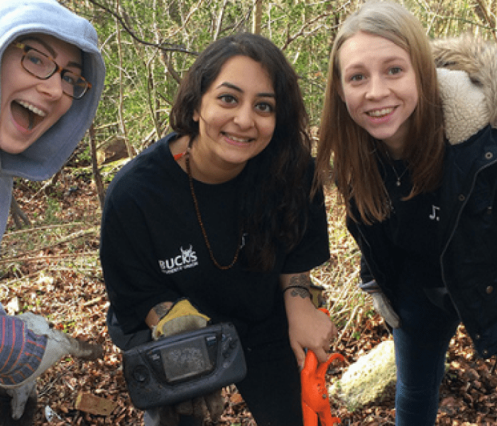Three BNU students stood posing for a photo in the woods whilst holding a metal detector