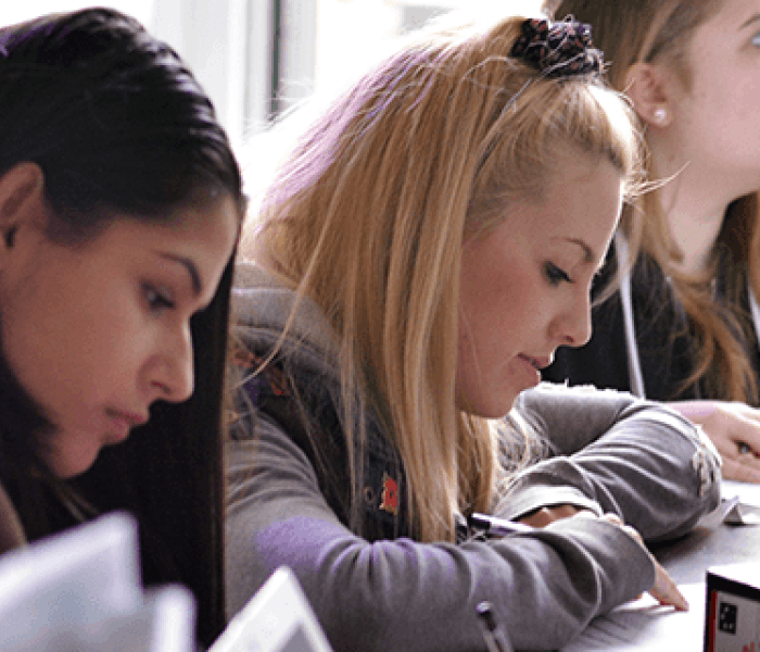 Three BNU students sat at a table sat next to one another taking notes on paper