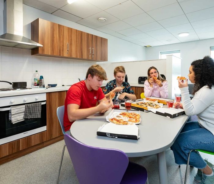 four students eating pizza at a kitchen table in Windsor House accommodation