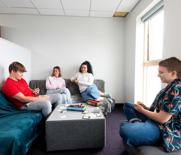 Four students playing a board game in a lounge area in Windsor House accommodation