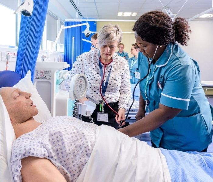 A BNU student nurse alongside a hospital bed which has a male dummy in