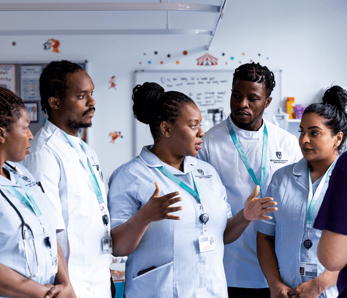 Five student nurses stood in conversation with a lecturer in a nursing simulation suite 