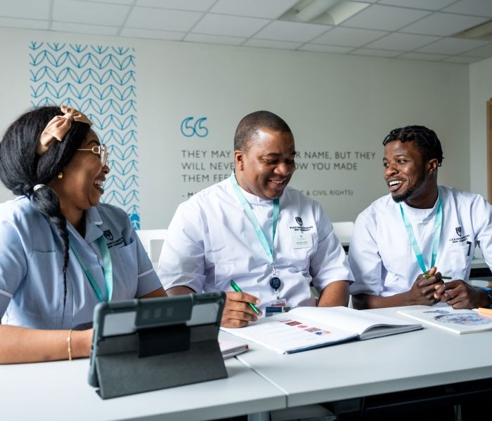 Three nursing students sat at a table next to one another looking at a textbook