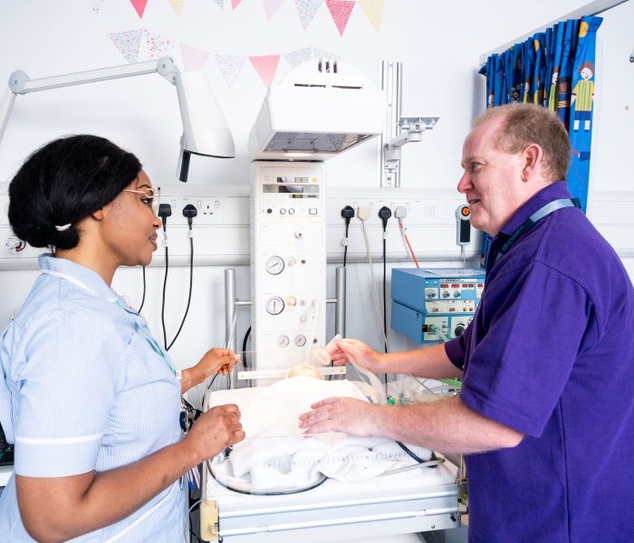 A student nurse stood in a simulation ward next to a lecturer giving words of advice