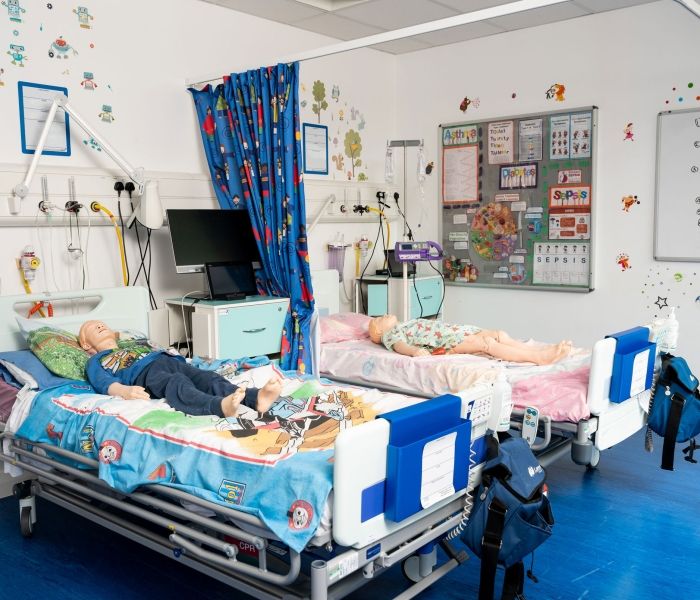 Two hospital beds in a simulation room with dummy children laying on them