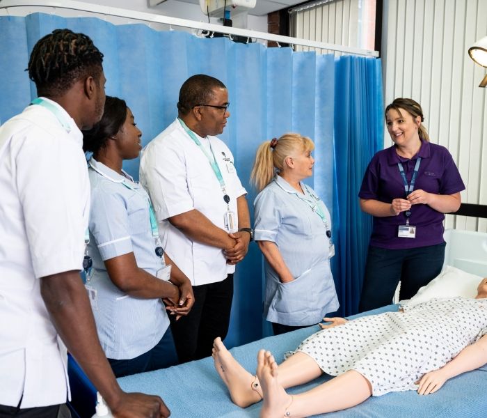 Four nursing students in uniform stood around a simulated hospital bed as a dummy child lays on the bed