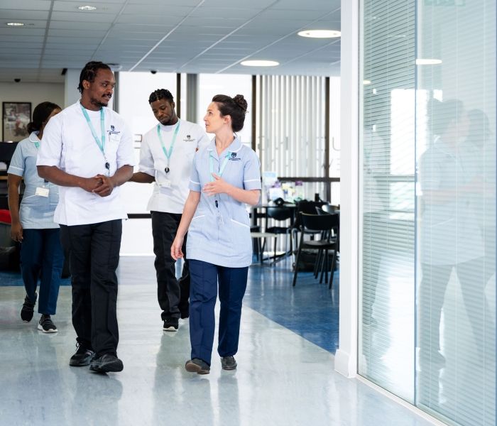 Two nursing students in uniform walk down a corridor whilst in discussion with one another