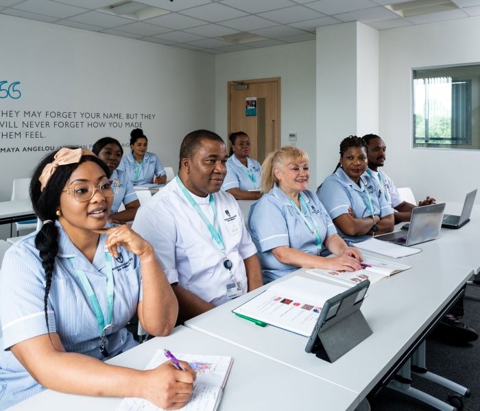 Eight nursing students sat in their uniform in a classroom facing the front of the room with textbooks open