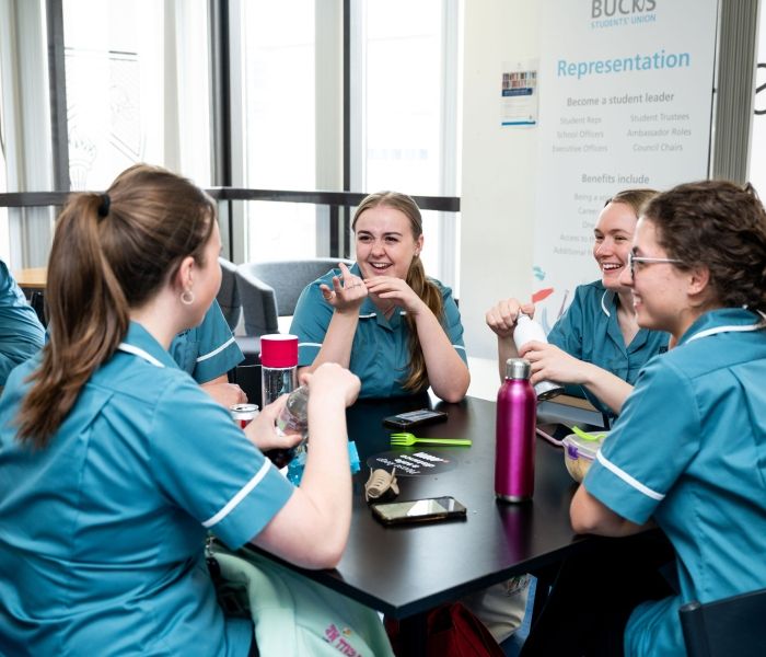 Five nursing students sat around a square table enjoying a break whilst in conversation