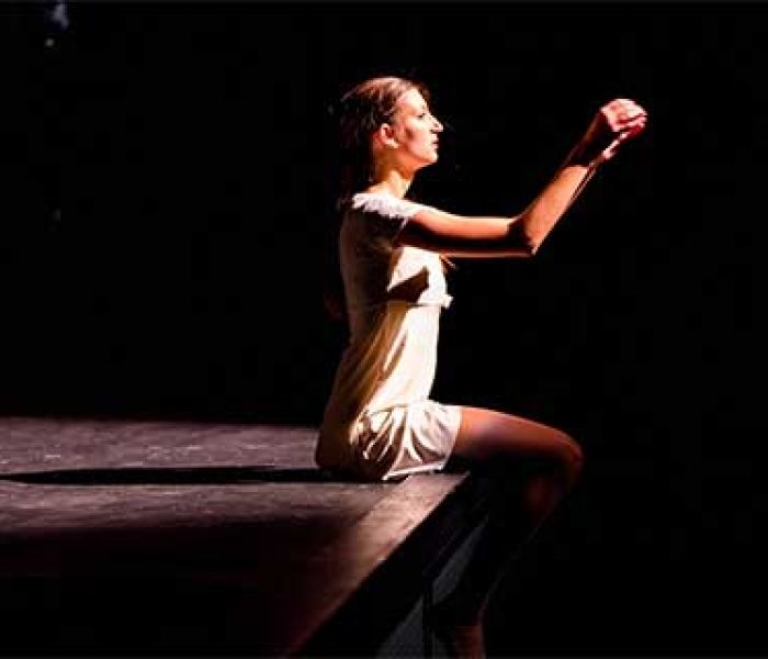 Musical Theatre student sat on a stage in the spotlight