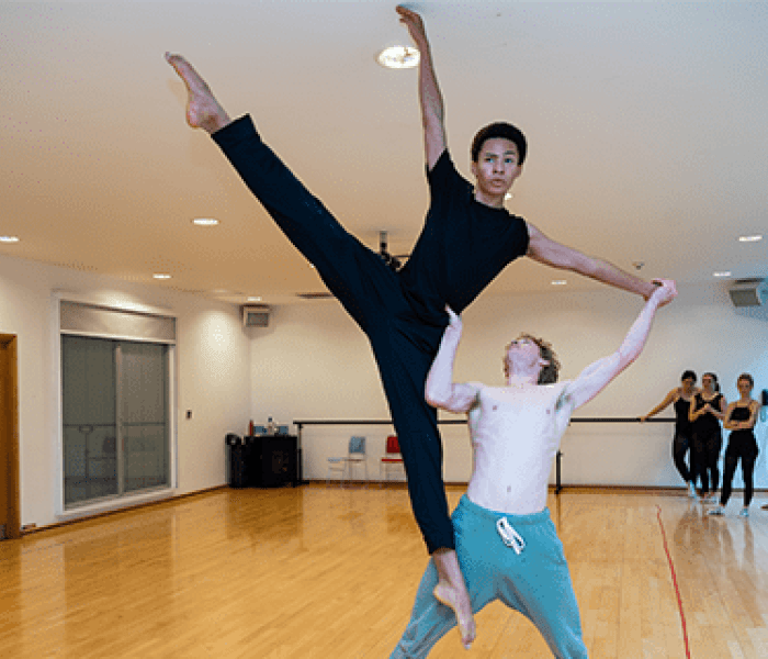 A dance student holding a fellow dance student up in the air as they perform a routine