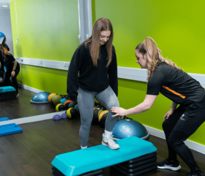 A woman lifting her leg onto a step as she undergoes fitness testing from a member of BNU staff.