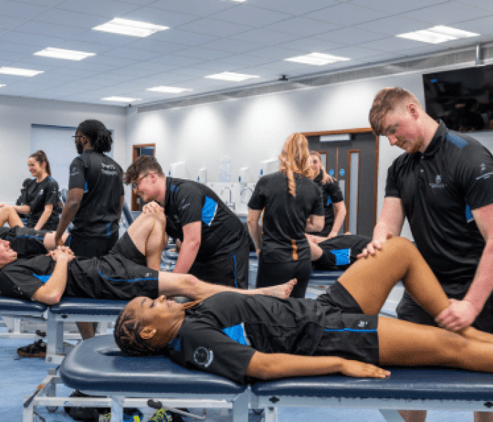 Sports Therapy students in uniform attending to a fellow student laying on a bed