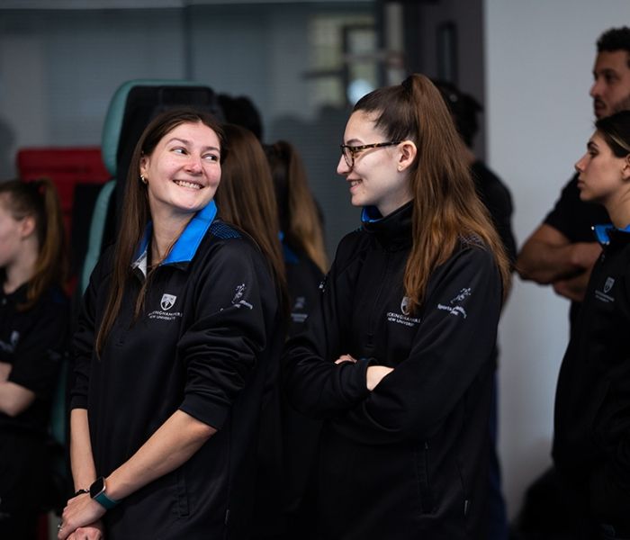 Two Sports Therapy students in uniform looking and smiling at one another