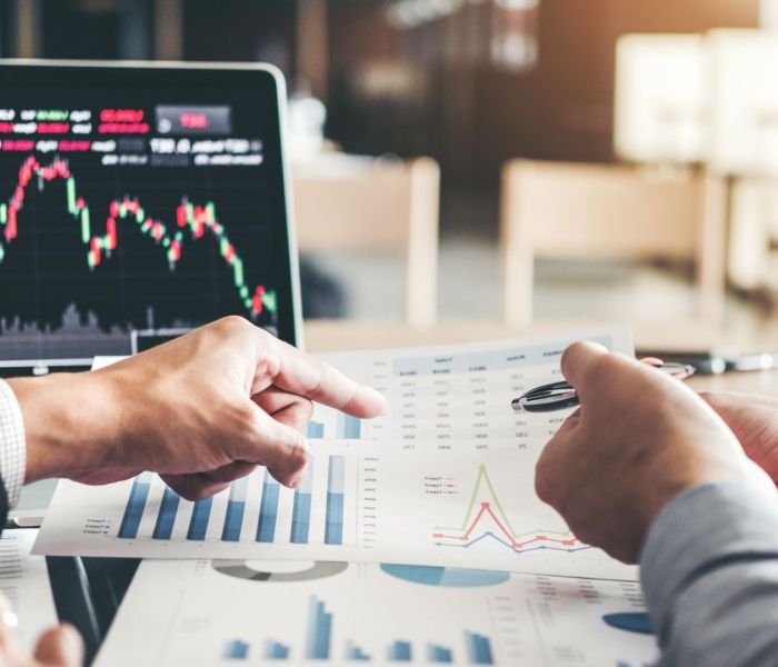 Two hands looking at data on a bit of paper with a laptop in the background.