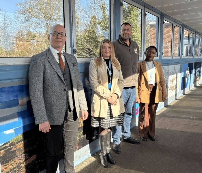 Four people stood together on a train station bridge posing for a photo