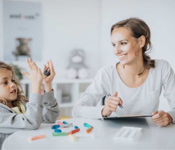 Occupational Therapist supporting a young child sat at a table through play therapy.