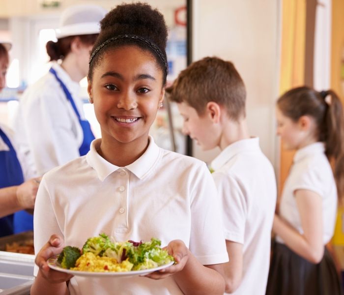 Child holding a plate of food in a school cafeteria
