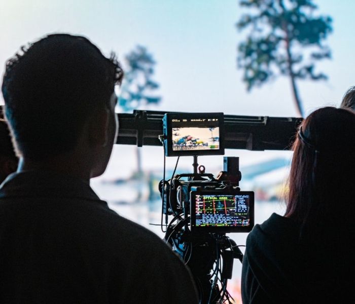 Silhouettes of two students facing a camera which is focusing on an LED screen wall.