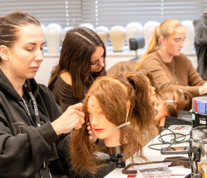 Hair and make-up students sat in a row in a classroom working on wigs.