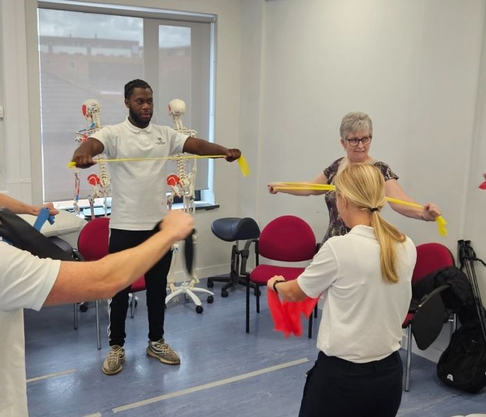 Five Physiotherapy students stood in a cricle pulling on resistance bands alongside a member of the public.