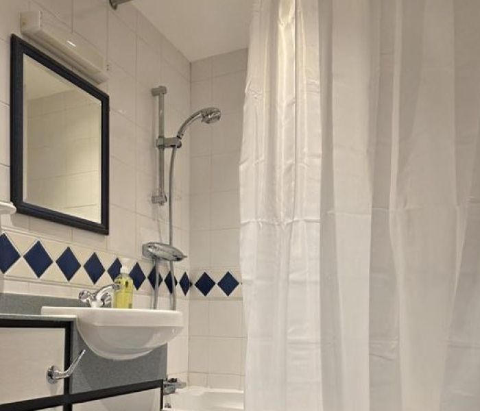 Bathroom interior at Alex House showing bathtub with shower head and shower curtain, sink and mirror
