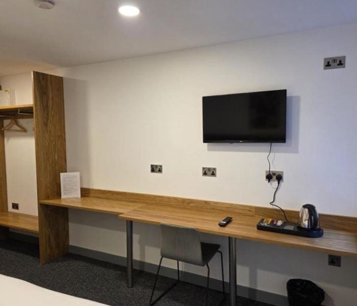Bedroom interior at Alex House showing desk with chair and kettle, wardrobe and wall-mounted TV