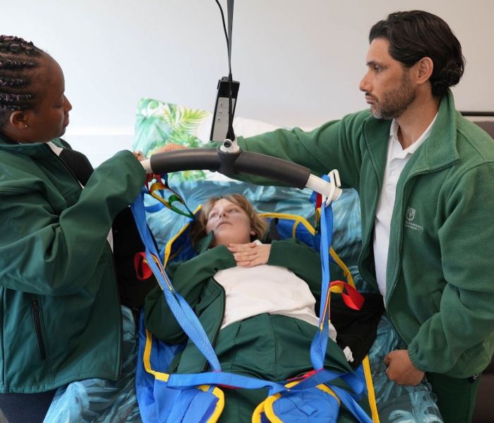 Occupational Therapy student in a hoist surrounded by two fellow students stood up either side.