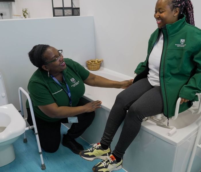 Two Occupational Therapy students in a bathroom. One sat on a seat in the bath and the other kneeling on the floor. 