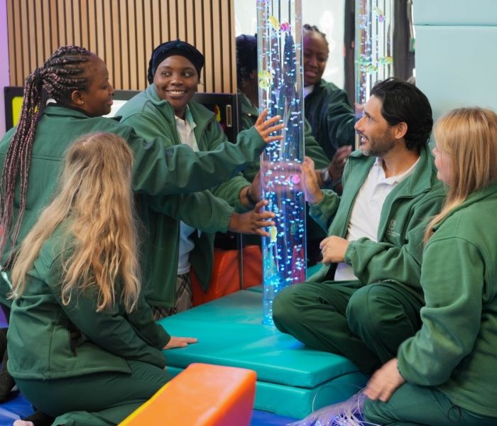 Four Occupational Therapy students in sensory room kneeling down looking at a water tube with lights in.