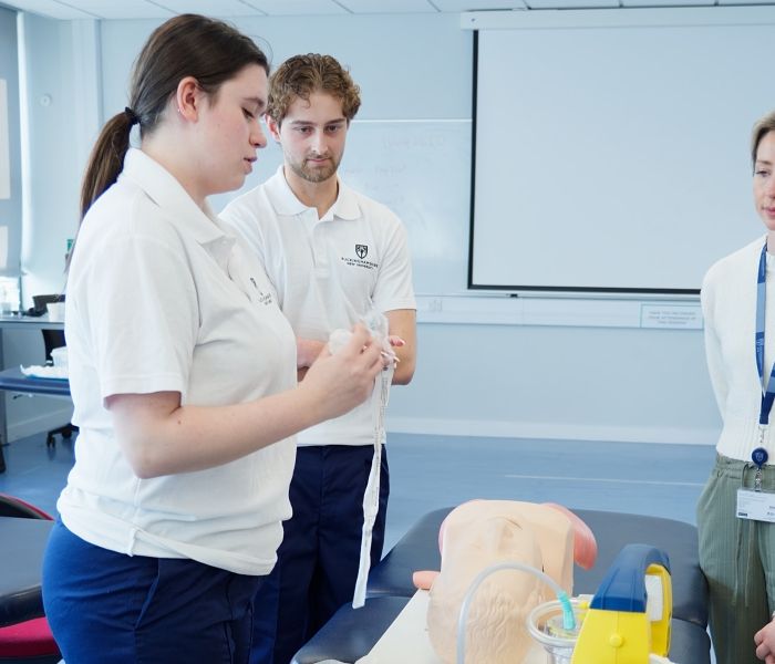 Physiotherapy students in white polo shirts practicing using medical suction equipment on a simulator mannequin during a practical session