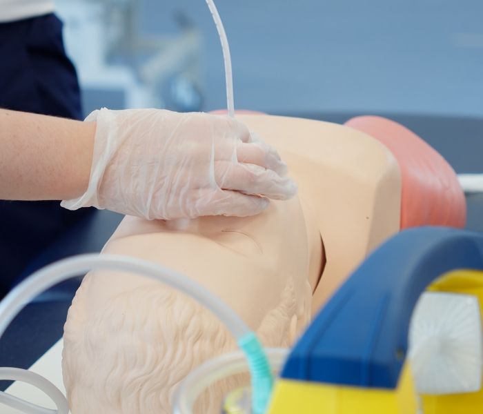 Close-up of a physiotherapy student with protective gloves practicing an airway management procedure on a training mannequin head