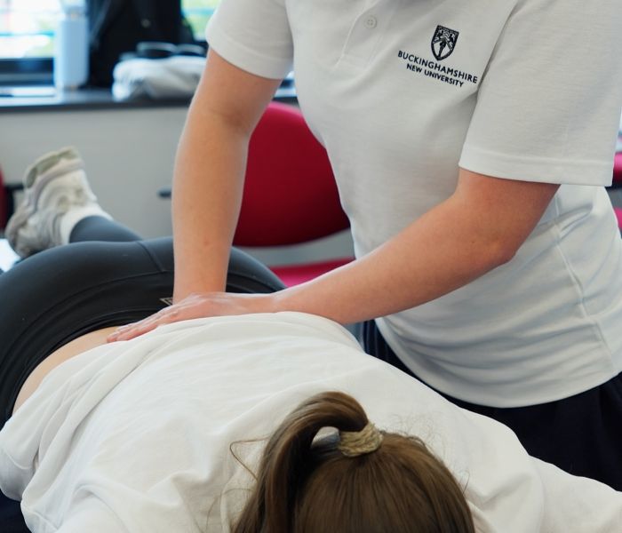 Physiotherapy student practicing lower back palpation and manual therapy techniques on a colleague lying face down on a treatment table