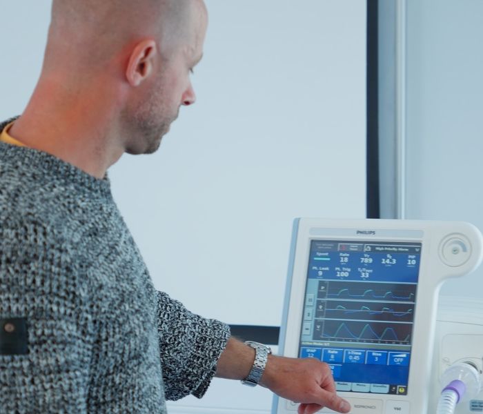 Physiotherapy lecturer stood up in a classroom and pushing the button on a clinical machine.