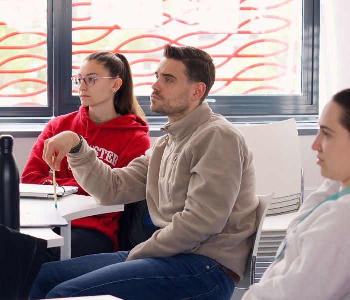 Three physiotherapy students sat around a table looking towards the front of a classroom