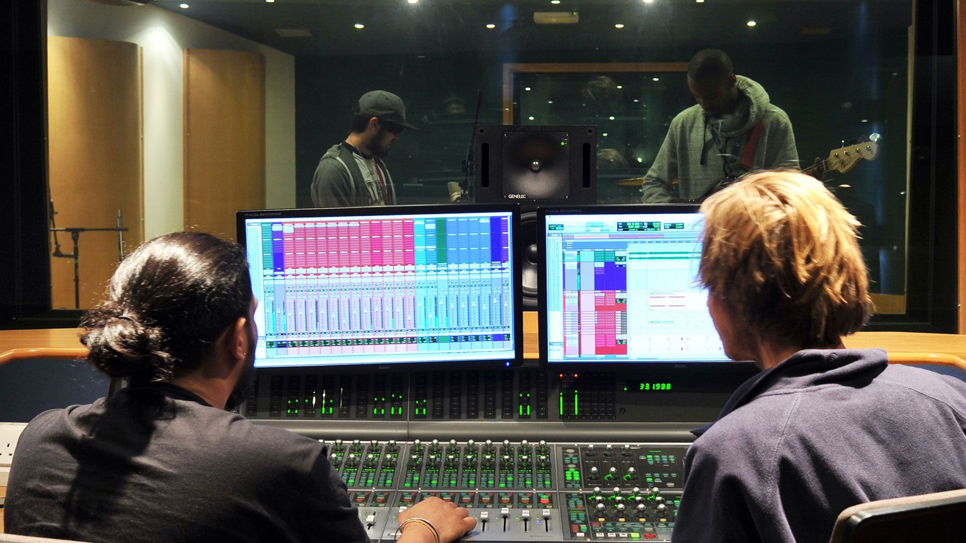 two men looking at two screens in a music studio 