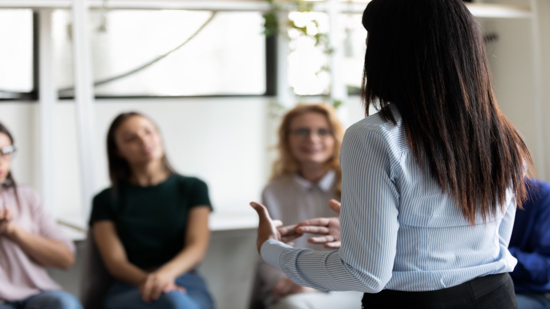 A woman with her back to the camera delivers a speech to three other females