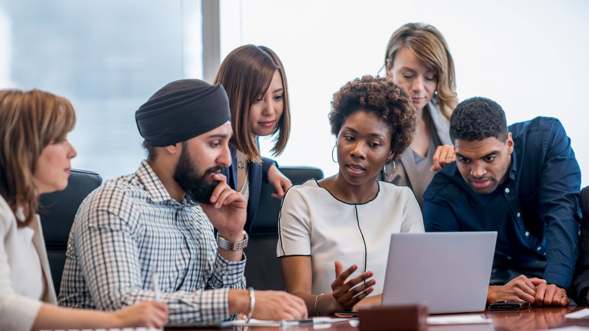 Diverse group of people sat looking at a laptop