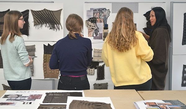 Four fashion design students looking at a wall with their work on
