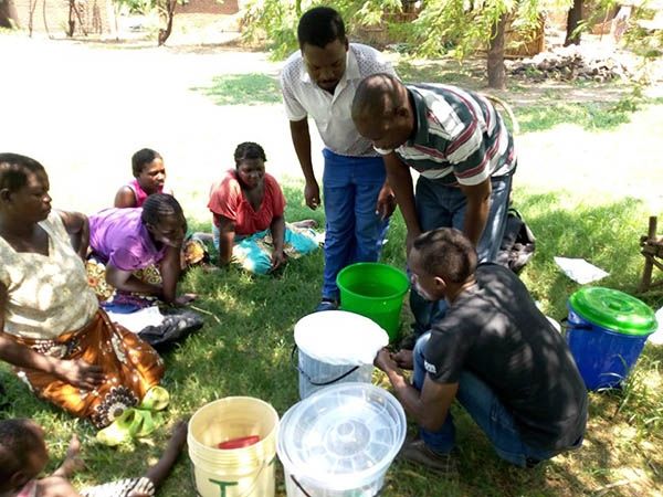 Adults and children leaning over to pick up buckets on the grass