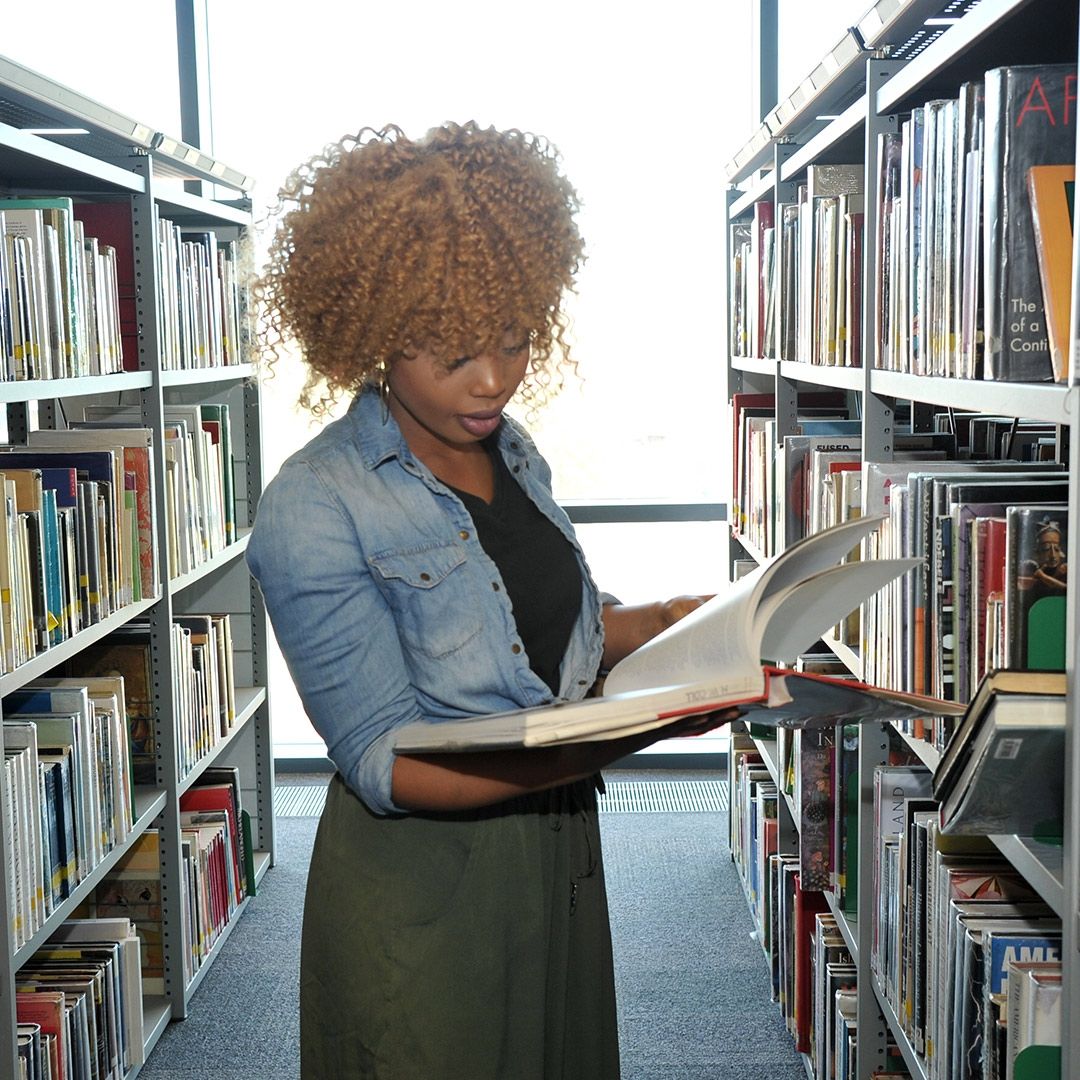 A lady reading a book standing up in the library