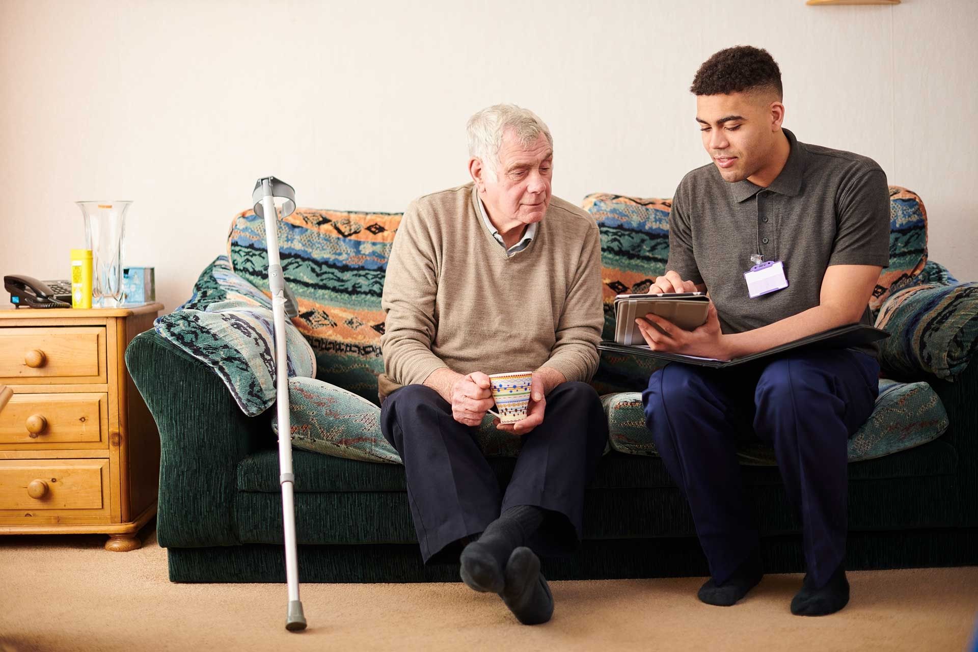 Senior man with crutch sitting with young male care worker