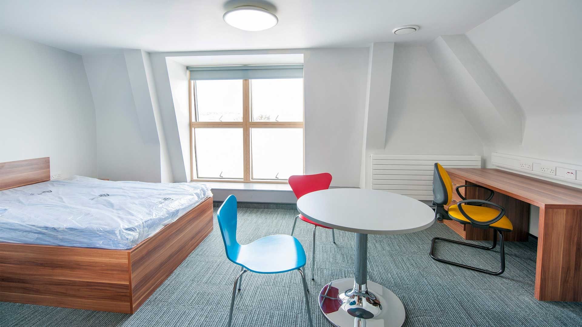 A bed, table, desk and chairs inside a Windsor House standard room accommodation