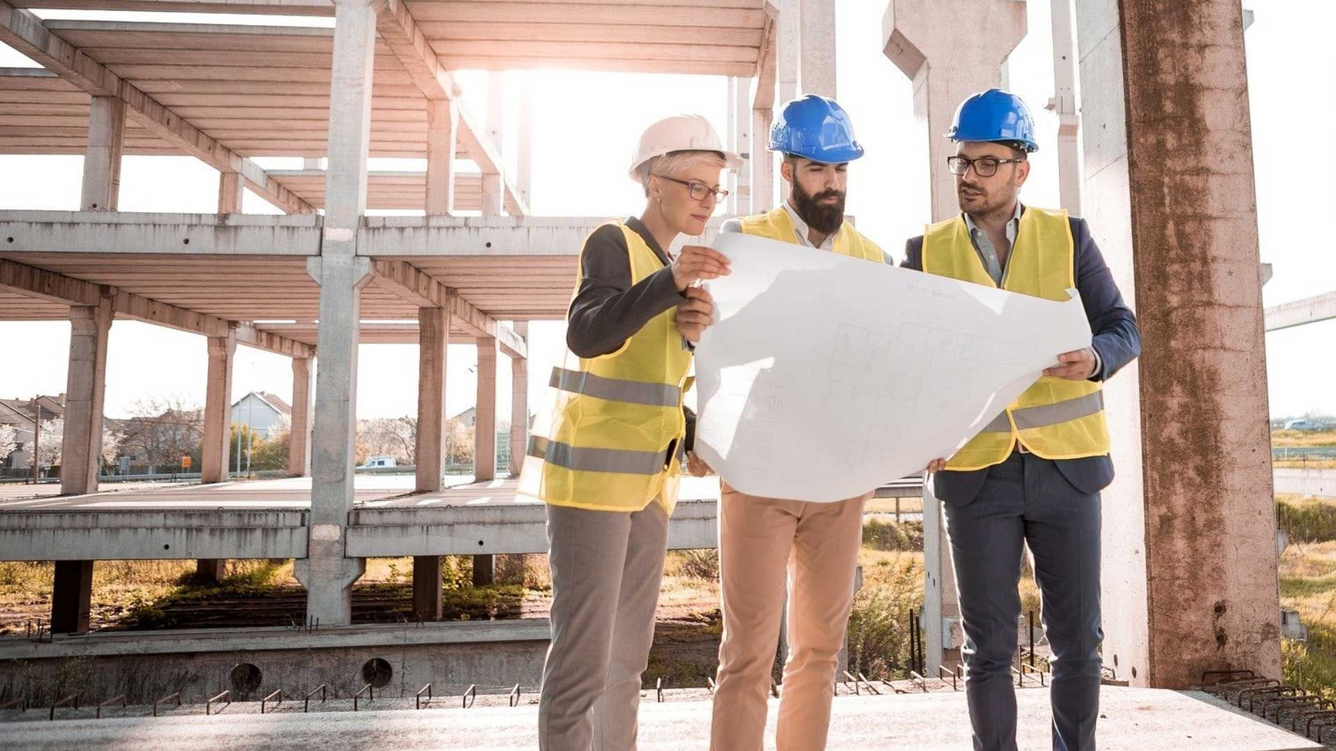Three people looking at a bit of paper on a construction site wearing high vis tops and hard hats