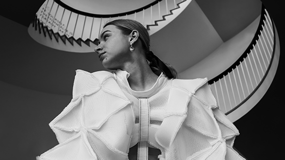 A BNU student looking to the side whilst wearing a fashionable outfit standing in front of a staircase in a black and white photo