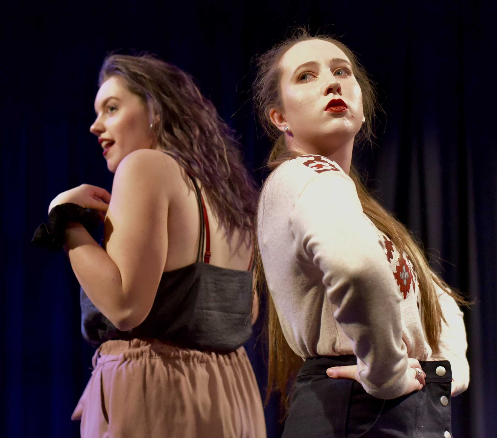 Two women back to back in the middle of a performance on stage